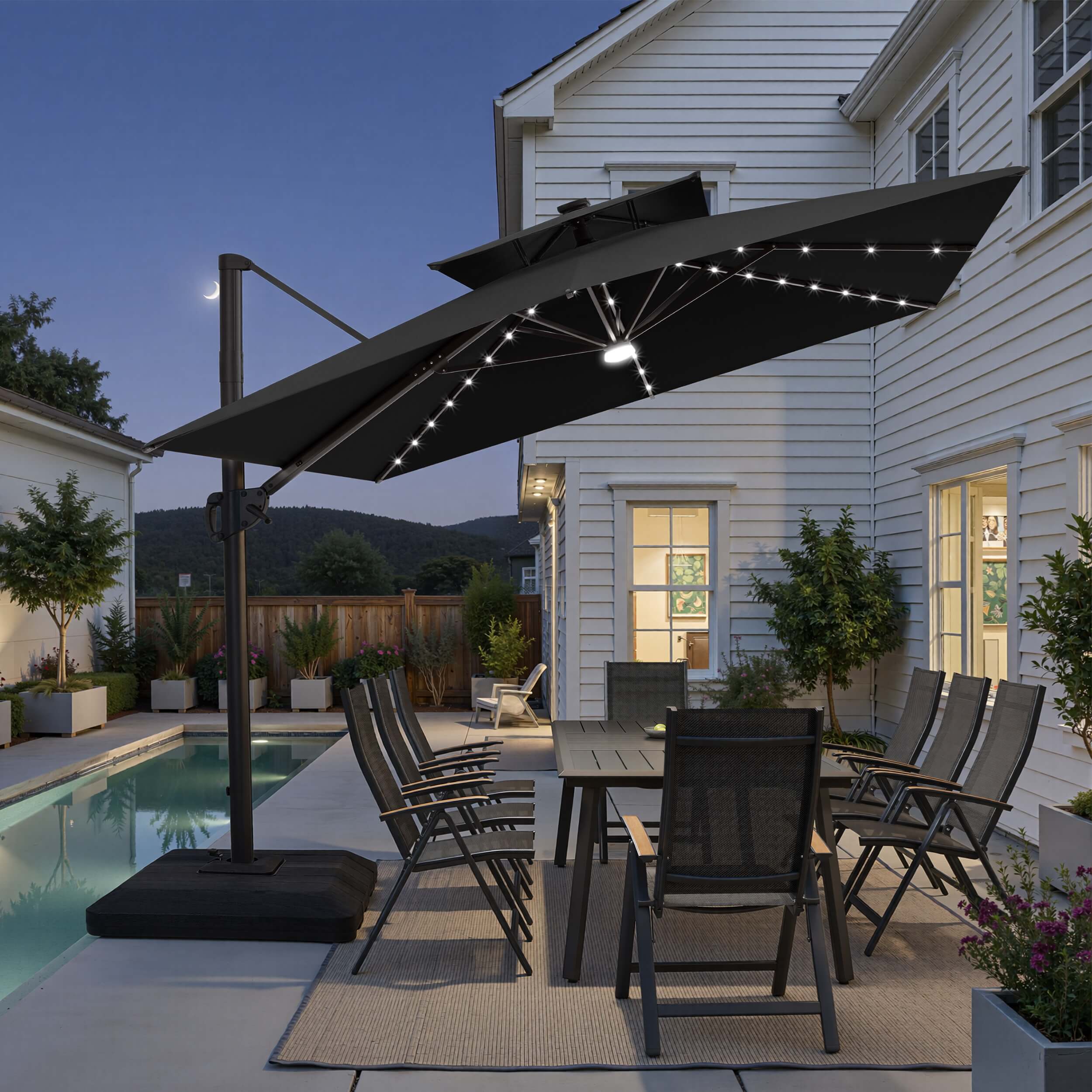 Tilted 12x9 ft black lighted cantilever umbrella with low-profile base shading a poolside dining set at twilight