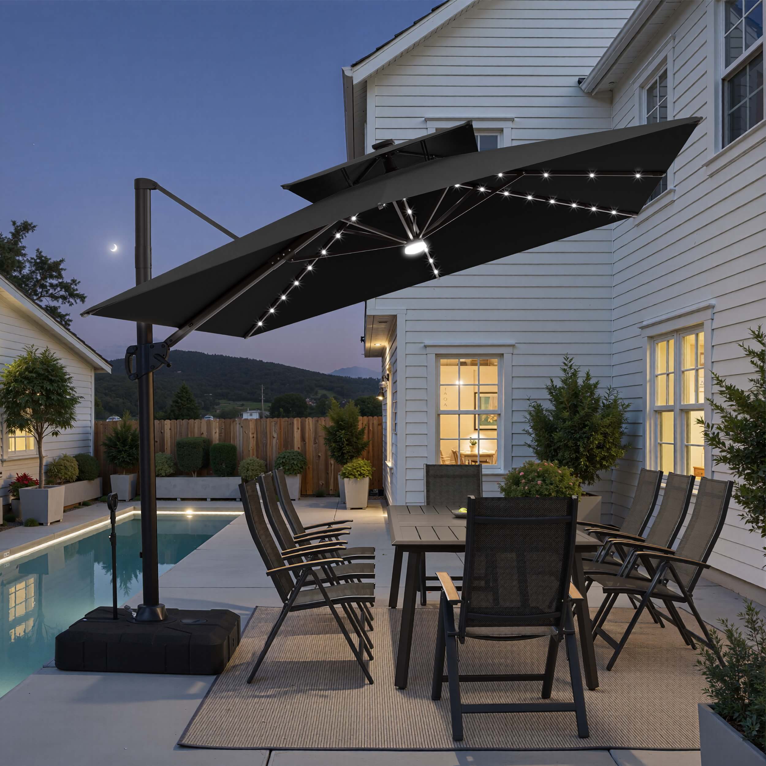 Tilted 12x9 ft black lighted cantilever umbrella with wheeled base shading a poolside dining set at twilight