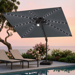 Tilted 12x9 ft grey lighted cantilever umbrella with heavy-duty base shading poolside lounge chairs at sunset